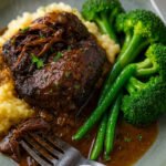 Plate of slow cooked beef cheeks on creamy mashed potatoes with rich gravy, broccolini and broccoli, from a Slow Cooked Beef Cheeks recipe.