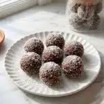 bliss balls recipe coated in desiccated coconut on a white plate